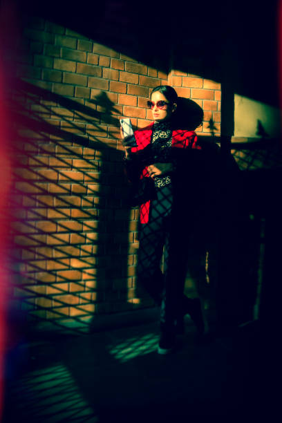 A stylish young woman stands in the sunlight and shade of the main entrance and uses her smartphone. The photo has been shot and processed to showcase the Lomo photography/Lomography style.