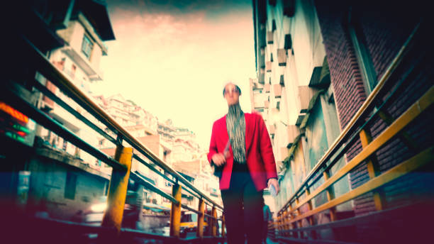 A trendy young woman prefers walking to reach her destination in the fifteen-minute city. She confidently walks on the footpath beside the main street of the busy town. This motion-blur image showcases the distinctive Lomo photography/Lomography style.