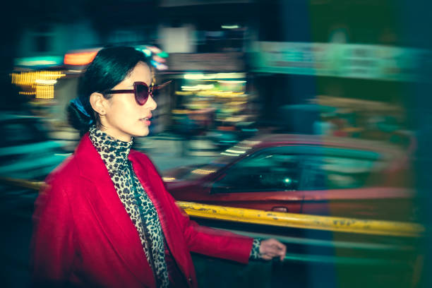 A trendy young woman prefers walking to reach her destination in the fifteen-minute city. She confidently walks on the footpath beside the main street of the busy town. This shutter drag image technique showcases the distinctive Lomo photography/Lomography style.