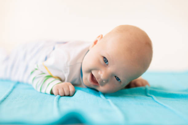 Adorable baby in white sunny bedroom. Newborn child relaxing in bed. Nursery for young children. Textile and bedding for kids. Family morning at home. New born kid during tummy time with toy bear.
