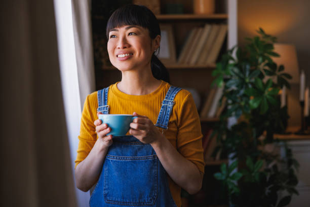 istock Woman standing by the window drinking coffee while relaxing at home 2199116629