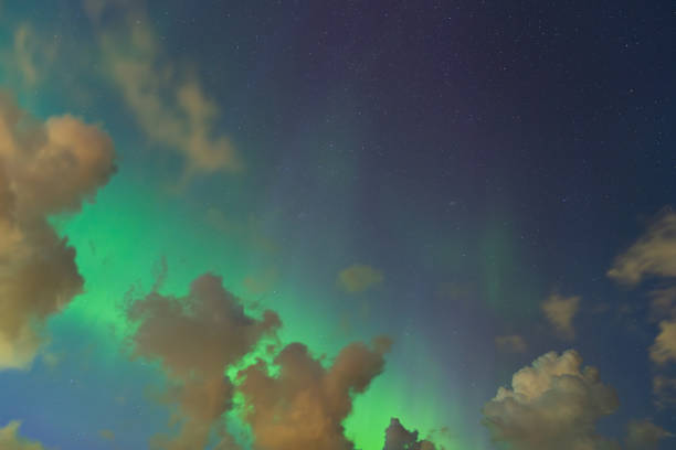 Aurora Borealis and Clouds: Shimmering green Northern Lights dance across a starry sky, illuminating dramatic clouds with vibrant color.