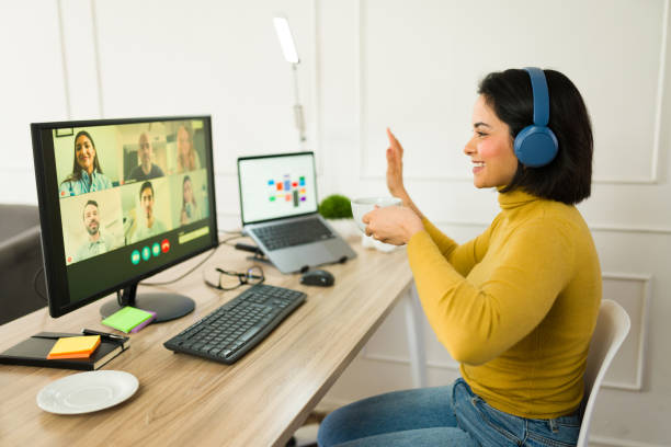 istock Smiling freelancer greeting remote colleagues during video conference, sipping coffee from home workspace 2199120064