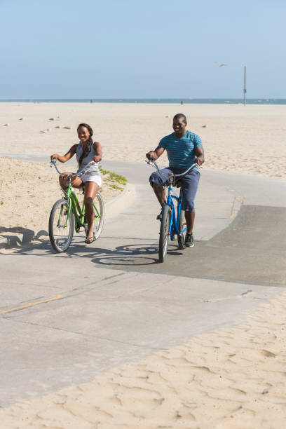 istock Young black couple on bikes at beach 2199121077
