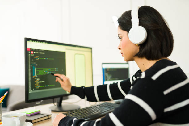 istock Young woman software developer wearing headphones working remotely and pointing at computer screen with lines of code 2199121332