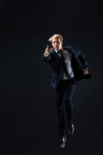 istock In a dark studio, a man in a sharp navy suit leaps mid-air, 2199124501