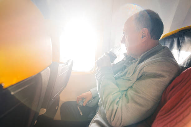 Senior man drinking water while looking out the window of an Airplane.