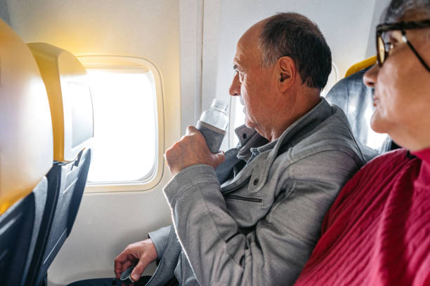 istock Senior Man Drinking Water While Looking Out The Window Of An Airplane 2199125794