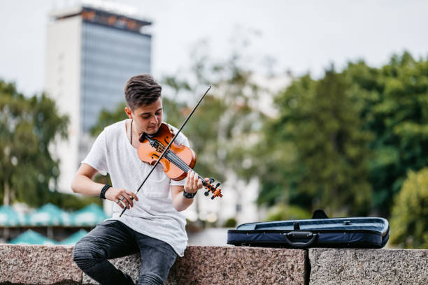 Handsome young man playing a violin for cash on the quayside.