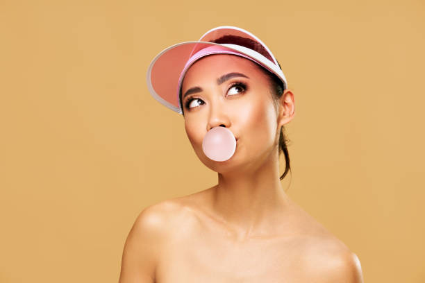 istock Trendy young woman blowing bubble gum on beige background. 2199128535