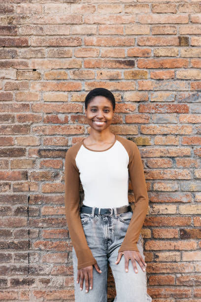 istock Young black woman smiling and leaning against brick wall 2199129410