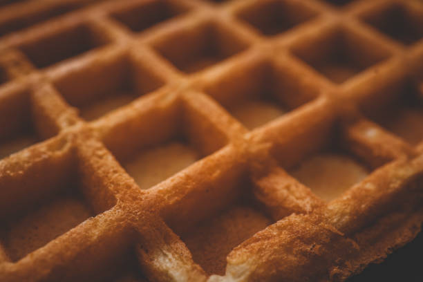 Golden-brown crispy waffles in a close-up shot. Detailed texture with a crisp outer layer and soft interior. Freshly baked breakfast food with a warm and inviting appearance