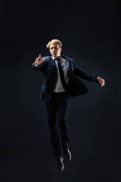 istock In a dark studio, a man in a sharp navy suit leaps mid-air, 2199131885