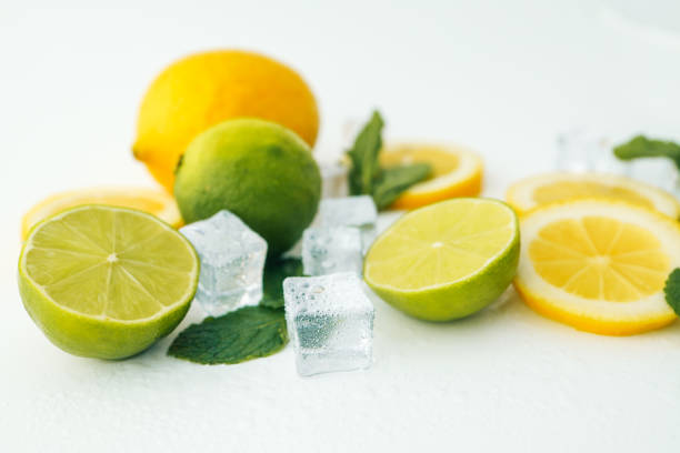 Fresh lime and lemon halves with mint leaves and ice cubes on a white background. A vibrant composition showcasing citrus fruits, perfect for healthy food, drinks, or summer themes.