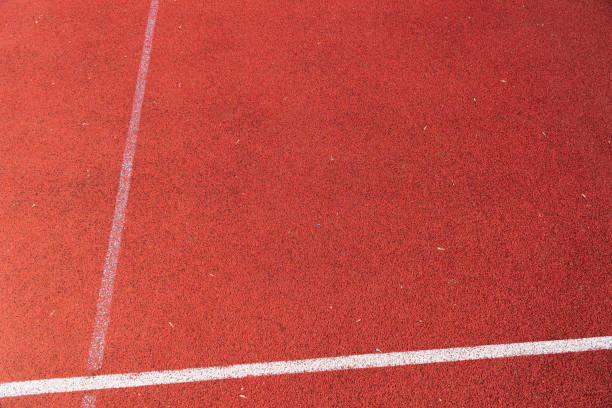 Red rubberized track with white lane markings under clear skies surrounded by natural elements during daylight hours.