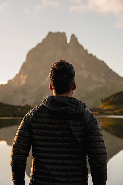 istock Man in front of a mountain lake at sunrise 2199132887