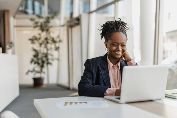 mujer de negocios sonriendo mientras trabaja en su computadora portátil - usar el ordenador fotografías e imágenes de stock
