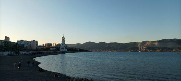 Russia, Novorossiysk- May 27, 2022: A serene coastal landscape featuring a rocky beach bathed in the soft hues of twilight, with gentle waves washing over the shore. The beautiful church in the background adds to the tranquility of the atmosphere