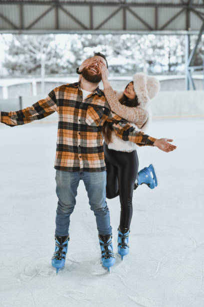 istock Affectionate Girlfriend Teasing Boyfriend Covering His Eyes While Skating on Ice Rink 2199136983