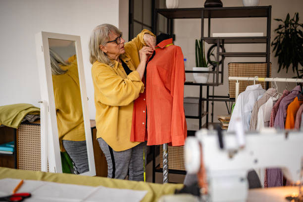 istock Senior woman tailoring a vibrant shirt in her home-based design studio while showcasing her creativity and craftsmanship 2199138856
