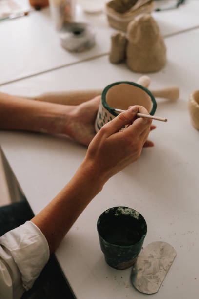 istock Experienced artist painting designs on ceramic cup in pottery workshop. Potter draws an abstract design into earthenware cup. 2199139162