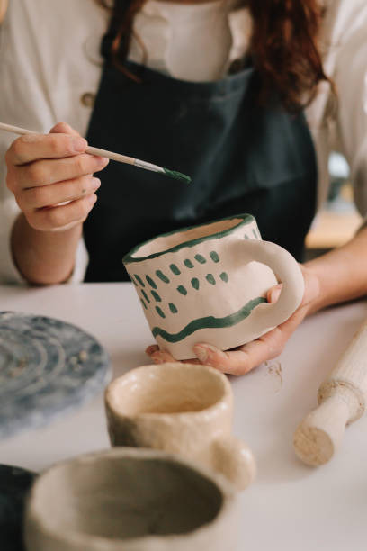 istock Experienced artist painting designs on ceramic cup in pottery workshop. Potter draws an abstract design into earthenware cup. 2199139284