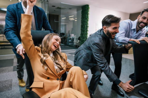 istock Playful scene in a modern office with businesspeople engaging in a friendly competition. In the image, colleagues are playfully pushing each other on office chairs. 2199139565
