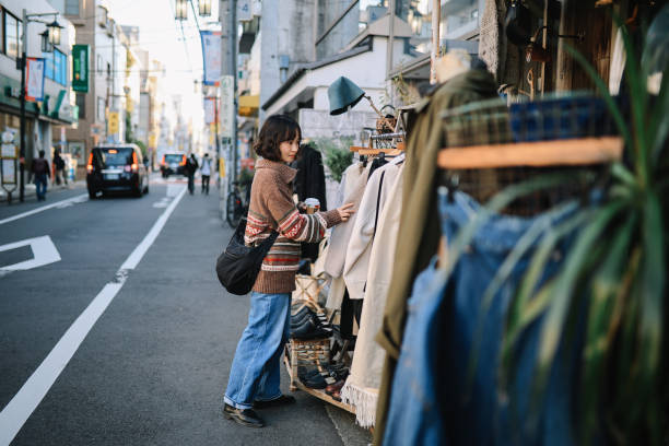 Fashionable Japanese woman in her 30s having a relaxed day in Tokyo. She is browsing through the hip vintage stores, looking for some clothing while having a coffee to go. Lifestyle, street style and sustainable shopping concepts in Tokyo.