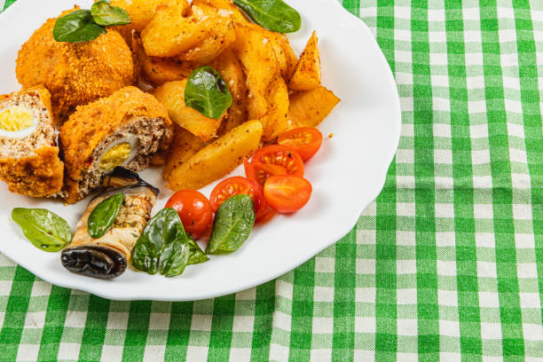A colorful plate features crispy breaded meat next to golden potatoes and cherry tomatoes, garnished with fresh spinach leaves. This meal showcases vibrant flavors and textures.