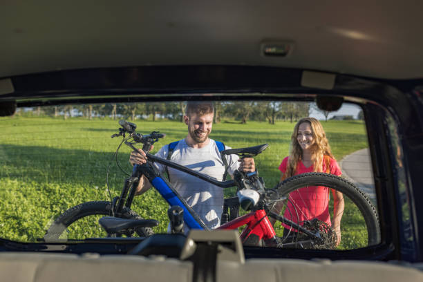 Young man is unloading electric mountain bikes, for himself and his girlfriend, lifting them from the hitch rack on the vehicle.