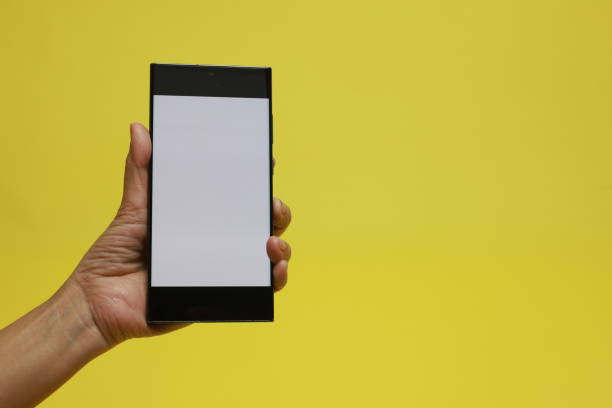 A woman's hands holding a smartphone mockup with a chroma key white screen isolated over a yellow  background
