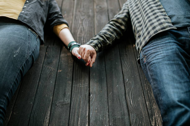 A couple stands side by side on a rustic wooden background, holding hands as a symbol of love, trust, and connection. A candid, intimate moment that captures the essence of togetherness.
