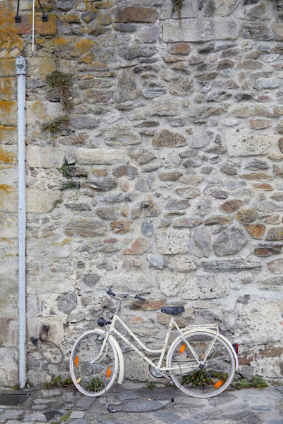 Charming scene in a quiet alleyway in Passau, Germany, featuring a single bicycle leaning against an ancient white stone wall. The narrow passageway, framed by historic architecture and weathered cobblestones, evokes a timeless European ambiance of simplicity and nostalgia