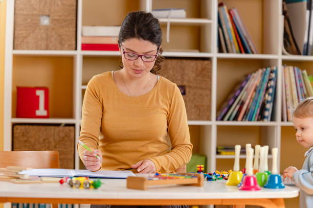 istock A preschool teacher in a mustard sweater reviews a lesson plan in a notebook, surrounded by educational toys and materials in a well-organized classroom 2199174310
