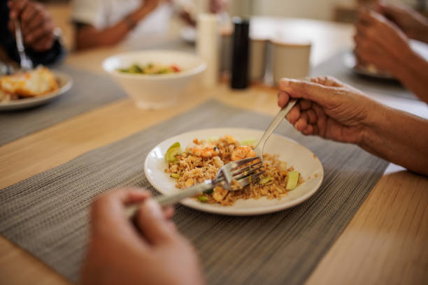Unrecognizable senior Thai couples sit together at a dining table in a warm and inviting dining room, enjoying lunch and engaging in conversation.