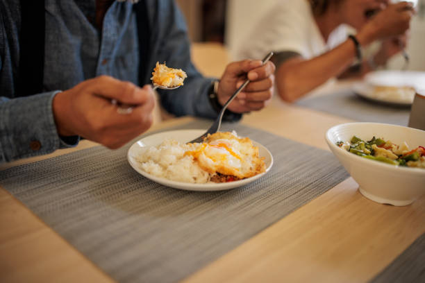 Mature Thai man and woman share a pleasant lunch together at the dining table in their home.