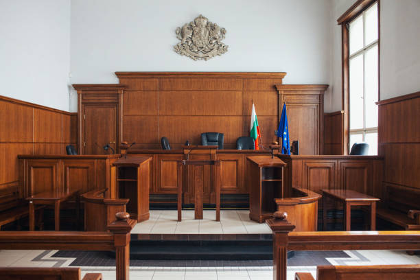Editorial image showcasing the interior of a courtroom in Sofia, Bulgaria. The space is characterized by elegant wooden paneling and traditional furnishings, with the Bulgarian coat of arms prominently positioned above the judge's bench. Flanking the bench are the national flag of Bulgaria and the European Union flag, representing the principles of justice and governance. The absence of people in the courtroom emphasizes its architectural beauty and formal atmosphere, making it a striking representation of the judicial system in Bulgaria.