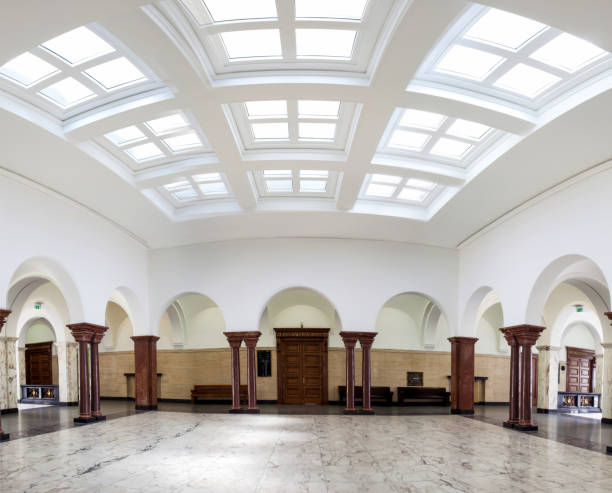 Editorial image showcasing the stunning interior panorama of the Sofia Courthouse, located in Bulgaria's capital. This expansive hall is characterized by its soaring ceilings adorned with intricate moldings and large skylights that flood the space with natural light, highlighting the polished marble floors. The design features classical columns and elegant arched doorways, emphasizing the courthouse's rich historical and judicial heritage. The tranquil yet authoritative ambiance reflects the building's pivotal role in Bulgaria's legal framework. Perfect for editorial use, this image captures the essence of Bulgarian architecture and the judicial environment.