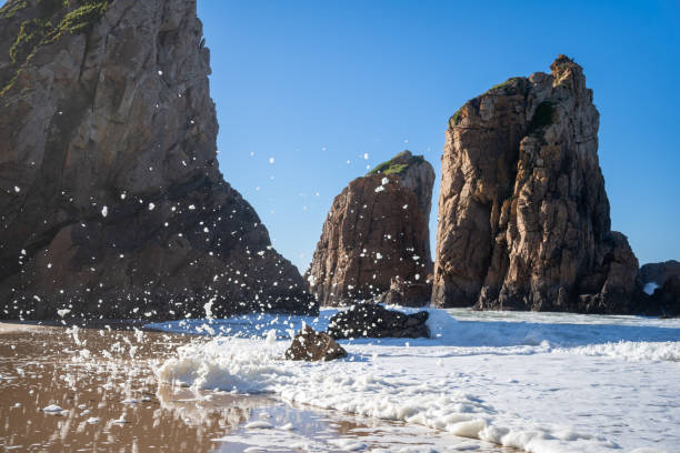 Golden cliffs and textured rock walls frame a small sandy beach at Praia da Ursa, Cabo da Roca, with the Atlantic Ocean rushing through a rocky passage.