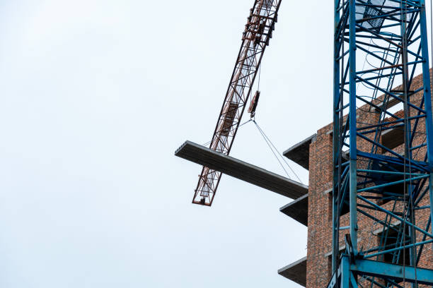 istock A crane is lifting a concrete slab to a multi-story building under construction, set against a cloudy sky backdrop 2199191348