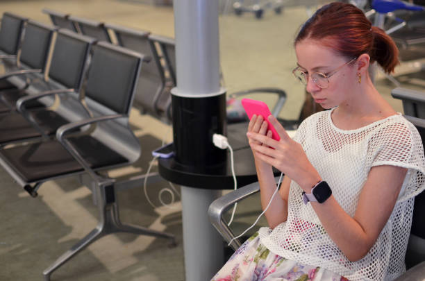 istock Teenage girl using smartphone while charging at airport terminal 2199200731