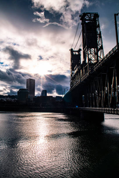 Color Photograph of Old Town in Portland, Oregon with the Willamette River and Steel Bridge in the foreground with a partly cloudy sky.