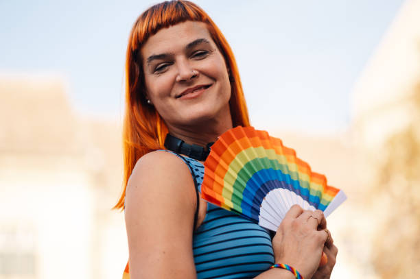 Redhead transgender activist smiling and holding a rainbow fan while participating in a pride parade, celebrating lgbtq plus rights and community