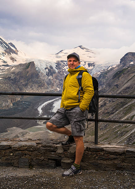 istock Middle-aged man stands on observation deck overlooking Grossglockner Mountain and Pastersee Glacier in Hohe Tauern National Park, Austria. Concept: travel, outdoor activities. 2199270287