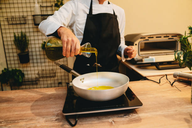 Chef pouring olive oil from a bottle into a frying pan, beginning the process of preparing a delicious meal on a kitchen counter