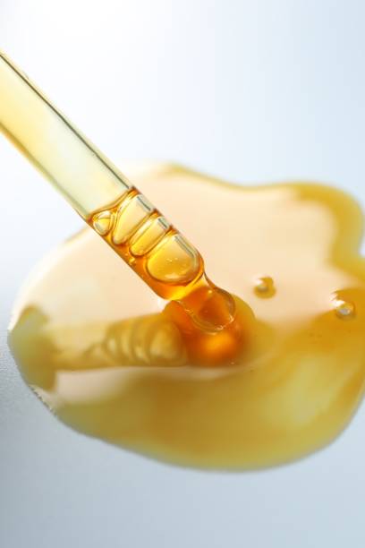 Dripping moisturizing serum from pipette on light grey background, closeup