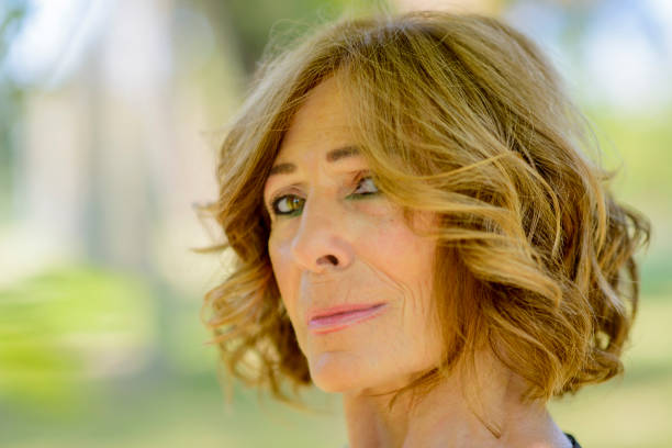 Middle aged woman smiles happily in a sunny park, exuding confidence and peace in nature. She looks chic and carefree in an elegant dress, surrounded by greenery. Perfect for lifestyle concepts