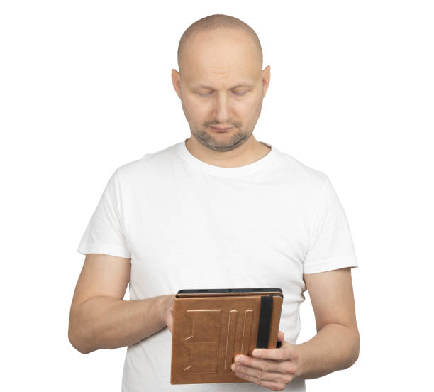 istock Middle-aged bald man in white t-shirt using a tablet with brown cover 2199278991