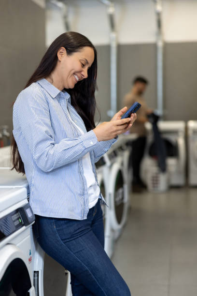 istock Woman using her phone while waiting washing clothes at the laundromat 2199284941