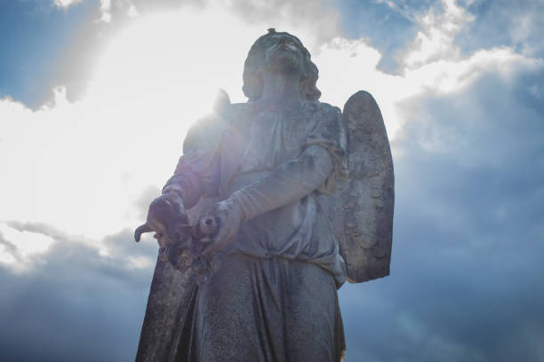 Dublin, Ireland - September 21, 2018: A weathered angel statue with one wing and a broken hand stands in Glasnevin Cemetery under a cloudy sky.